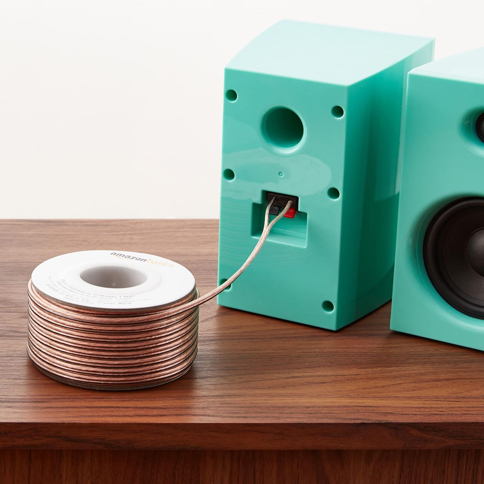 Amazon Basics 16-Gauge Speaker Wire placed on a wooden table with speakers